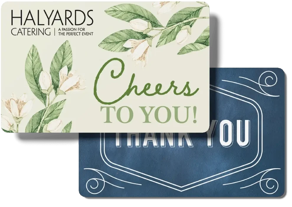 Two stacked Halyards Restaurant Group gift cards — one with floral design saying "Cheers to You!" from Halyards Catering, and a second dark blue "Thank You" card — representing gift card options available for all affiliated restaurants.