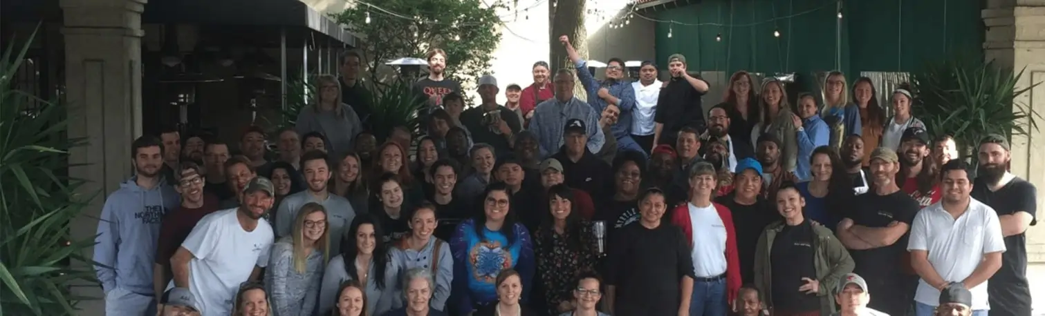 Large group photo of the Halyard Restaurant Group team smiling together outside under string lights, representing a welcoming and united work environment.
