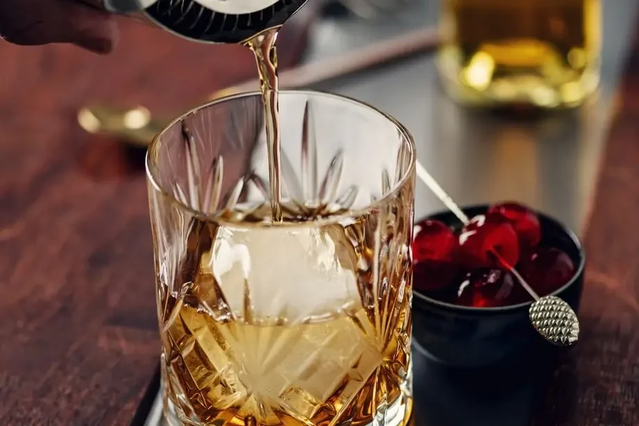 Whiskey cocktail with a large ice cube being prepared at Agio Bar, representing the classic cocktails menu